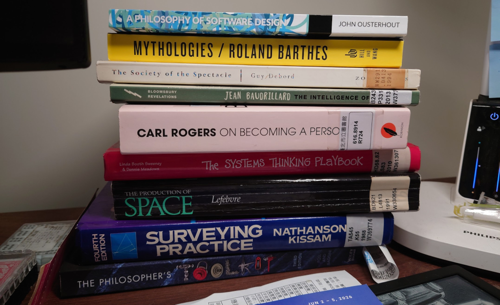 A pile of books on my table, from A Philosophy of Software Design, Surveying Practice, The Systems Design Playbook, The Society of the Spectacle and more